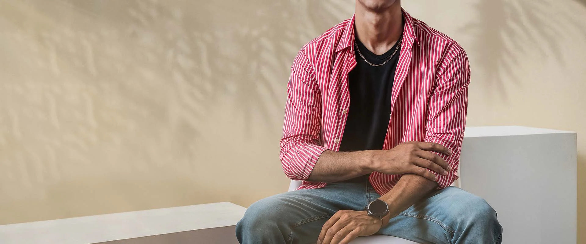Man sitting on a white bench wearing a pink striped shirt and blue jeans.